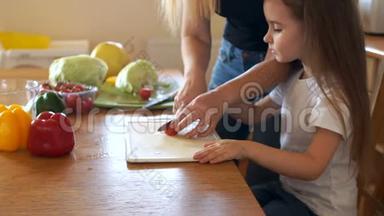 关爱的母亲教她的小女儿切蔬菜做沙拉。 素食，樱桃番茄
